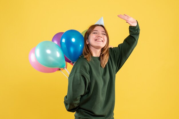 Vorderansicht junge Frau, die bunte Luftballons hinter ihrem Rücken versteckt