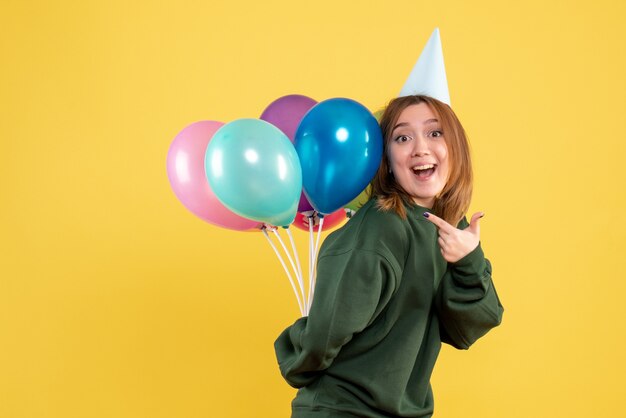 Vorderansicht junge Frau, die bunte Luftballons hinter ihrem Rücken versteckt