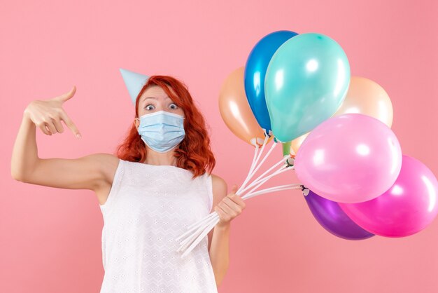 Vorderansicht junge Frau, die bunte Luftballons in Maske auf dem Rosa hält