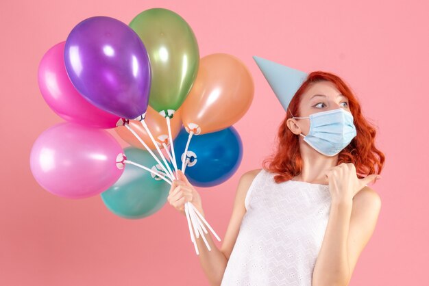 Vorderansicht junge Frau, die bunte Luftballons in Maske auf dem Rosa hält