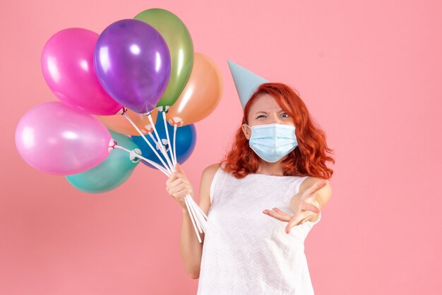 Vorderansicht junge Frau, die bunte Luftballons in Maske auf dem Rosa hält