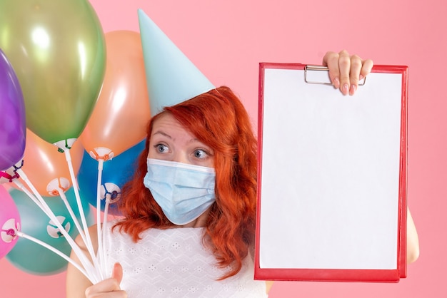 Kostenloses Foto vorderansicht junge frau, die bunte luftballons und aktennotiz auf rosa hält