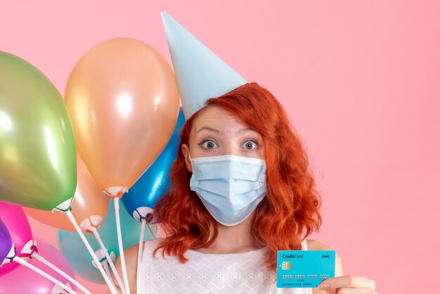 Vorderansicht junge Frau, die bunte Luftballons und Bankkarte auf Rosa hält