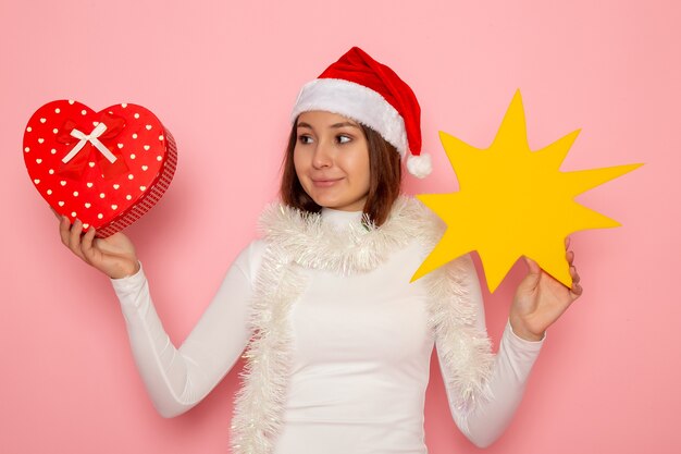 Vorderansicht junge Frau, die gelbe Figur hält und auf der rosa Wandschneeweihnachtsfarbfeiertags-Neujahrsmode präsentiert