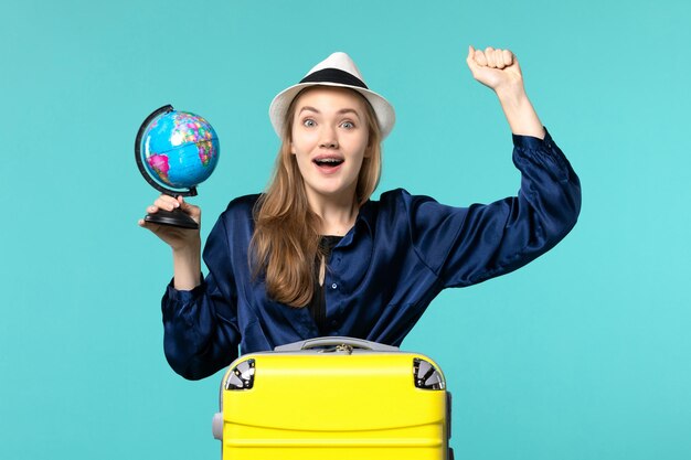 Vorderansicht junge Frau, die Globus hält und sich auf Urlaub auf weiblicher Reisereiseflugzeugurlaub des blauen Hintergrunds vorbereitet