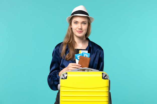 Vorderansicht junge Frau, die ihre Tickets hält und sich auf Reise auf dem blauen Hintergrundreiseflugzeug-Seeferienreisereise vorbereitet
