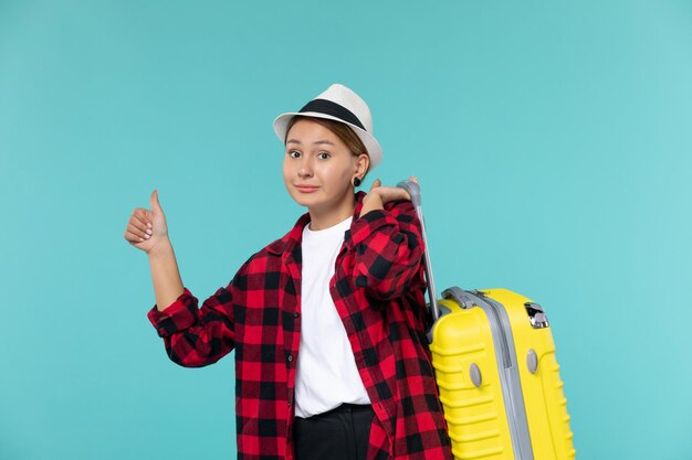 Vorderansicht junge Frau, die in den Urlaub mit ihrer gelben Tasche auf dem blauen Raum geht