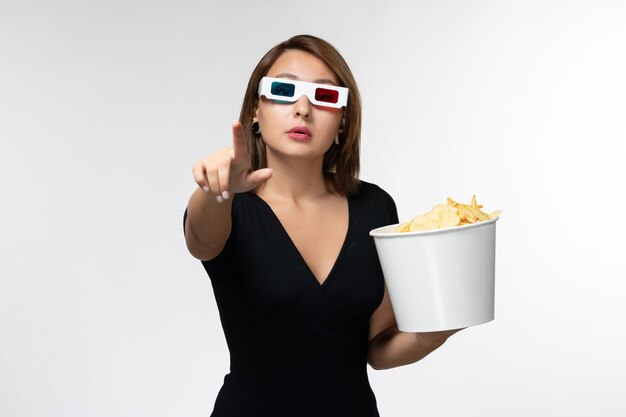 Vorderansicht junge Frau, die Kartoffelchips in d Sonnenbrille hält und Film auf hellweißer Oberfläche sieht