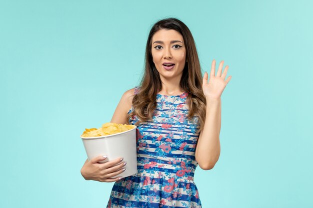 Vorderansicht junge Frau, die Korb mit Chips und Film auf blauer Oberfläche hält