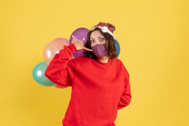 Vorderansicht junge Frau, die Luftballons in der sterilen Maske auf Gelb versteckt