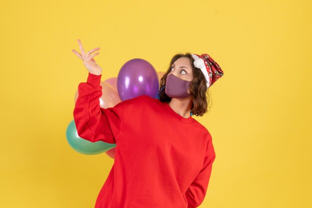 Vorderansicht junge Frau, die Luftballons in der sterilen Maske auf Gelb versteckt