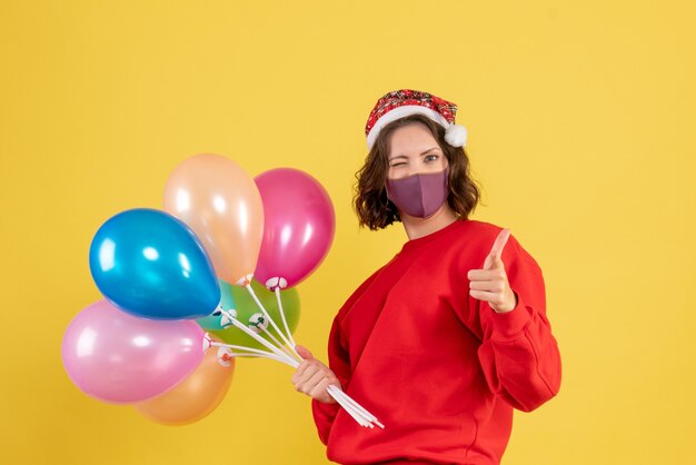 Vorderansicht junge Frau, die Luftballons in Maske auf Gelb hält