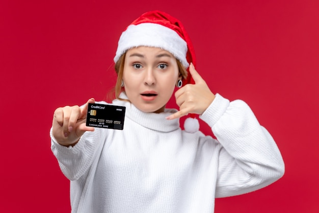 Vorderansicht junge Frau, die mit Bankkarte auf dem roten Hintergrund aufwirft