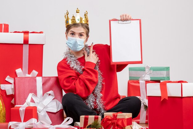 Vorderansicht junge Frau, die mit Weihnachtsgeschenken in der Maske sitzt