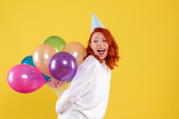 Vorderansicht junge Frau, die niedliche bunte Luftballons auf Gelb versteckt