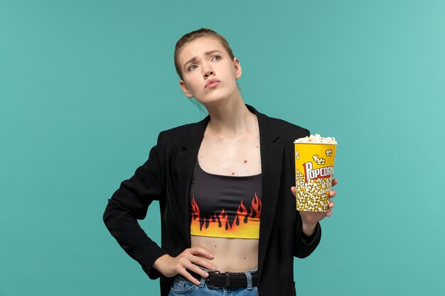 Vorderansicht junge Frau, die Popcorn isst und Film auf der blauen Oberfläche sieht