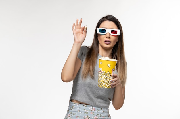 Vorderansicht junge Frau, die Popcorn isst und Film in d Sonnenbrille auf weißer Oberfläche sieht