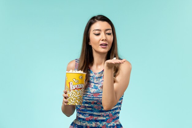 Vorderansicht junge Frau, die Popcorn-Paket auf dem blauen Schreibtisch hält