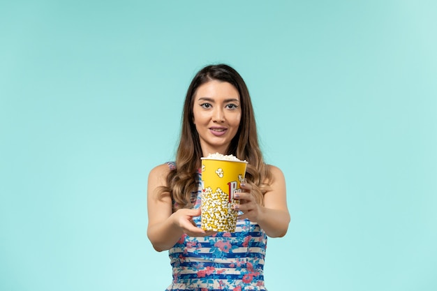 Vorderansicht junge Frau, die Popcorn-Paket auf hellblauem Schreibtisch hält
