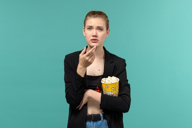 Vorderansicht junge Frau, die Popcorn-Paket hält Film auf hellblauer Oberfläche hält