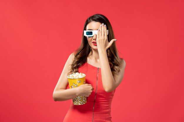 Vorderansicht junge Frau, die Popcorn-Paket in d Sonnenbrille auf dem roten Schreibtisch hält