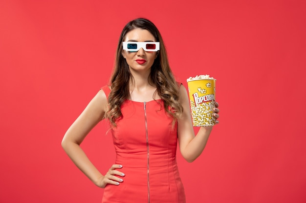 Vorderansicht junge Frau, die Popcorn-Paket in d Sonnenbrille auf der roten Oberfläche hält