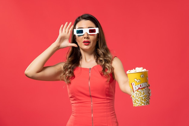 Vorderansicht junge Frau, die Popcorn-Paket in d Sonnenbrille auf hellroter Oberfläche hält