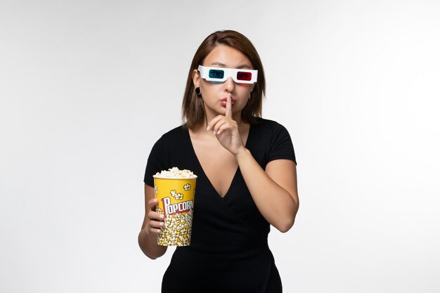 Vorderansicht junge Frau, die Popcorn-Paket in d Sonnenbrille hält und Film auf weißem Schreibtisch sieht
