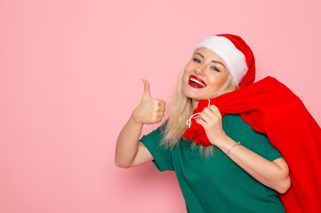 Vorderansicht junge Frau, die rote Tasche mit Geschenken auf der rosa Wandmodellfeiertagsweihnachtsfoto-Weihnachtsfärbung Santa trägt