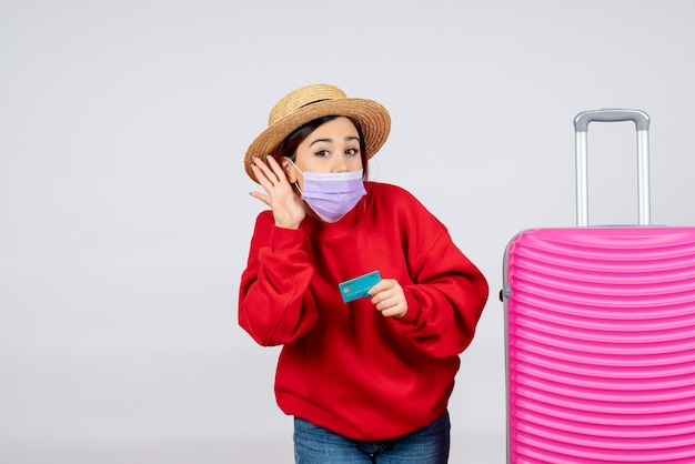 Vorderansicht junge Frau, die sich auf eine Reise in der Maske vorbereitet, die auf weißer Wand hört?