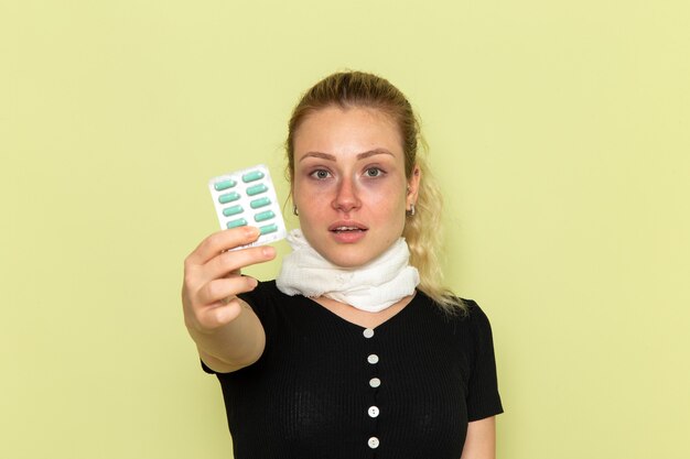 Vorderansicht junge Frau, die sich sehr krank und krank fühlt, hält Pillen auf der grünen Wandkrankheit weibliche Medizinkrankheit