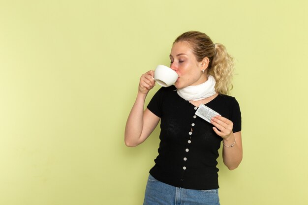 Vorderansicht junge Frau, die sich sehr krank und krank fühlt, Tasse Tasse Kaffee trinkend auf grüner Wandkrankheit Medizinkrankheit Gesundheit