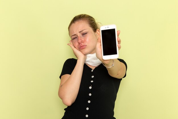 Vorderansicht junge Frau, die sich sehr krank und krank fühlt und ihr Telefon an der grünen Wandkrankheitsmedizin hält