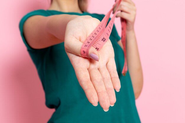 Vorderansicht junge Frau, die Taillenmaß auf der rosa Wandschönheitssportübungathletentraining schlank hält