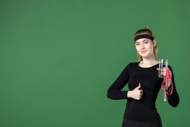 Vorderansicht junge Frau, die Taillenmaß und ein Glas Wasser auf grünem Hintergrund hält Farbe Gesundheit Körper schwarz Training Athlet Sport