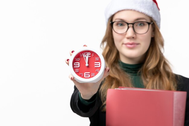 Vorderansicht junge Frau, die Uhr und Dateien auf weißen Wandlektionshochschulbüchern hält