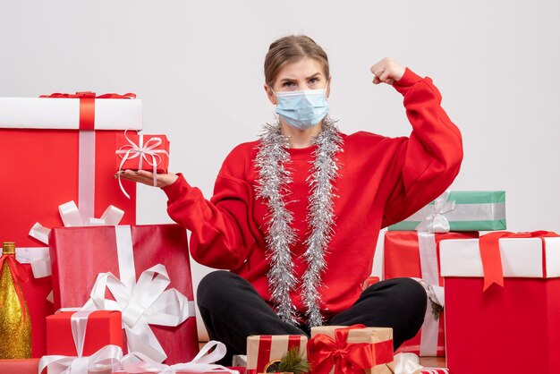 Vorderansicht junge Frau, die um Weihnachtsgeschenke in der sterilen Maske sitzt