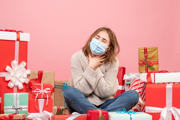 Vorderansicht junge Frau, die um Weihnachtsgeschenke in der sterilen Maske sitzt