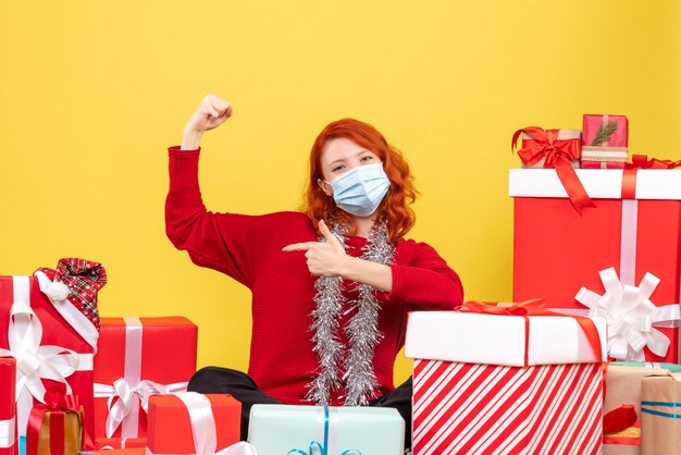 Vorderansicht junge Frau, die um Weihnachtsgeschenke mit Maske auf Gelb sitzt