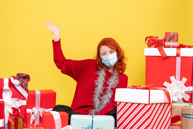 Vorderansicht junge Frau, die um Weihnachtsgeschenke mit Maske auf Gelb sitzt