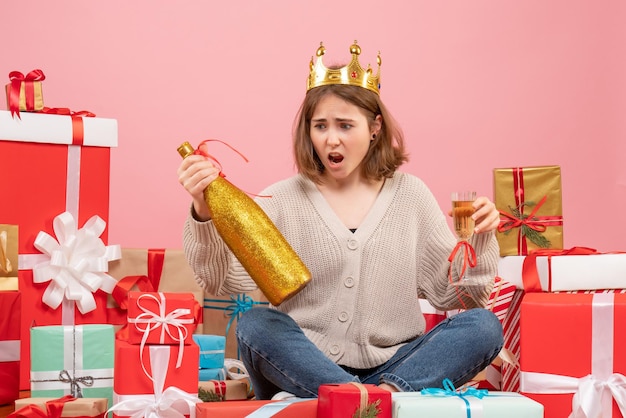 Vorderansicht junge frau, die um weihnachtsgeschenke sitzt, die mit champagner feiern