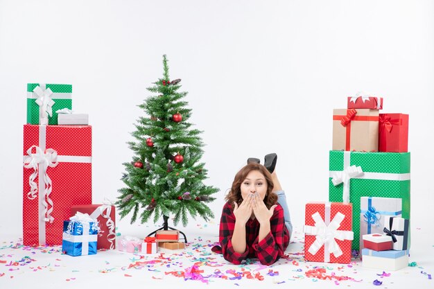 Vorderansicht junge Frau, die um Weihnachtsgeschenke und Feiertagsbaum auf weißem Boden Weihnachten Neujahrsgeschenkfarbe Schnee legt