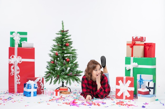 Vorderansicht junge frau, die um weihnachtsgeschenke und feiertagsbaum auf weißem hintergrund weihnachten neujahrsgeschenkfarbe schnee legt Kostenlose Fotos