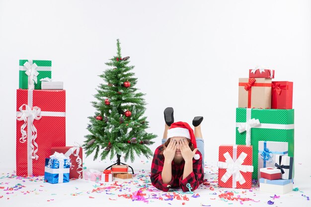 Vorderansicht junge Frau, die um Weihnachtsgeschenke und kleinen Feiertagsbaum auf dem weißen Hintergrund Weihnachten Neujahrsfarbschnee legt