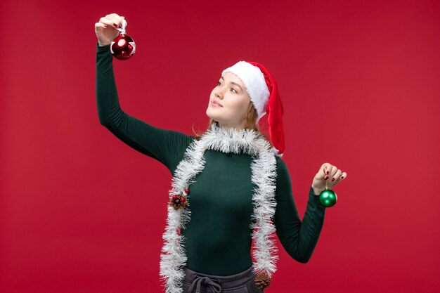 Vorderansicht junge Frau, die Weihnachtsbaumspielzeug auf dem roten Hintergrund hält