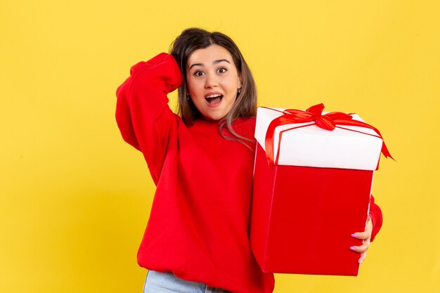 Vorderansicht junge Frau, die Weihnachtsgeschenk auf gelbem Hintergrund hält