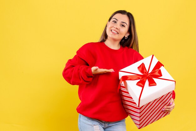 Vorderansicht junge Frau, die Weihnachtsgeschenk lächelnd auf gelbem Hintergrund hält