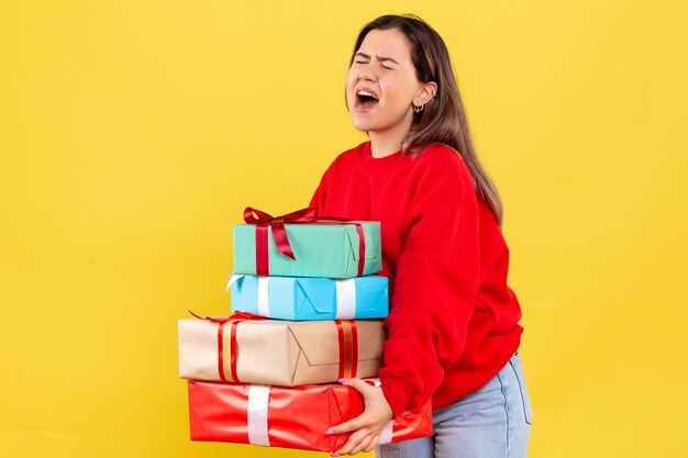 Vorderansicht junge Frau, die Weihnachtsgeschenke auf gelbem Boden Neujahrsmodellfarbe menschliches Weihnachtsgeschenk hält