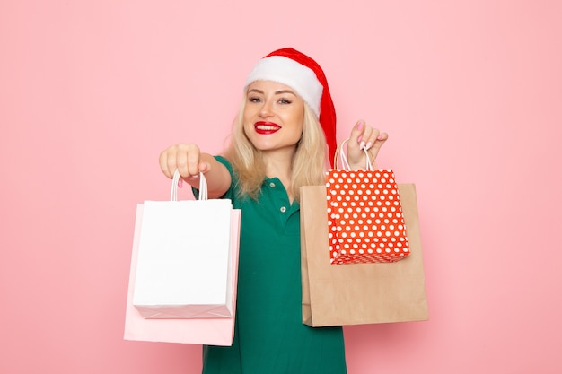 Vorderansicht junge Frau, die Weihnachtsgeschenke in Paketen auf den Neujahrsfeiertagen des rosa Wandweihnachtsfoto-Modells hält