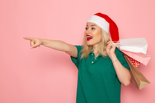 Vorderansicht junge Frau, die Weihnachtsgeschenke in Paketen auf rosa Wandmodellfeiertags-Weihnachtsneujahrsfarbe hält